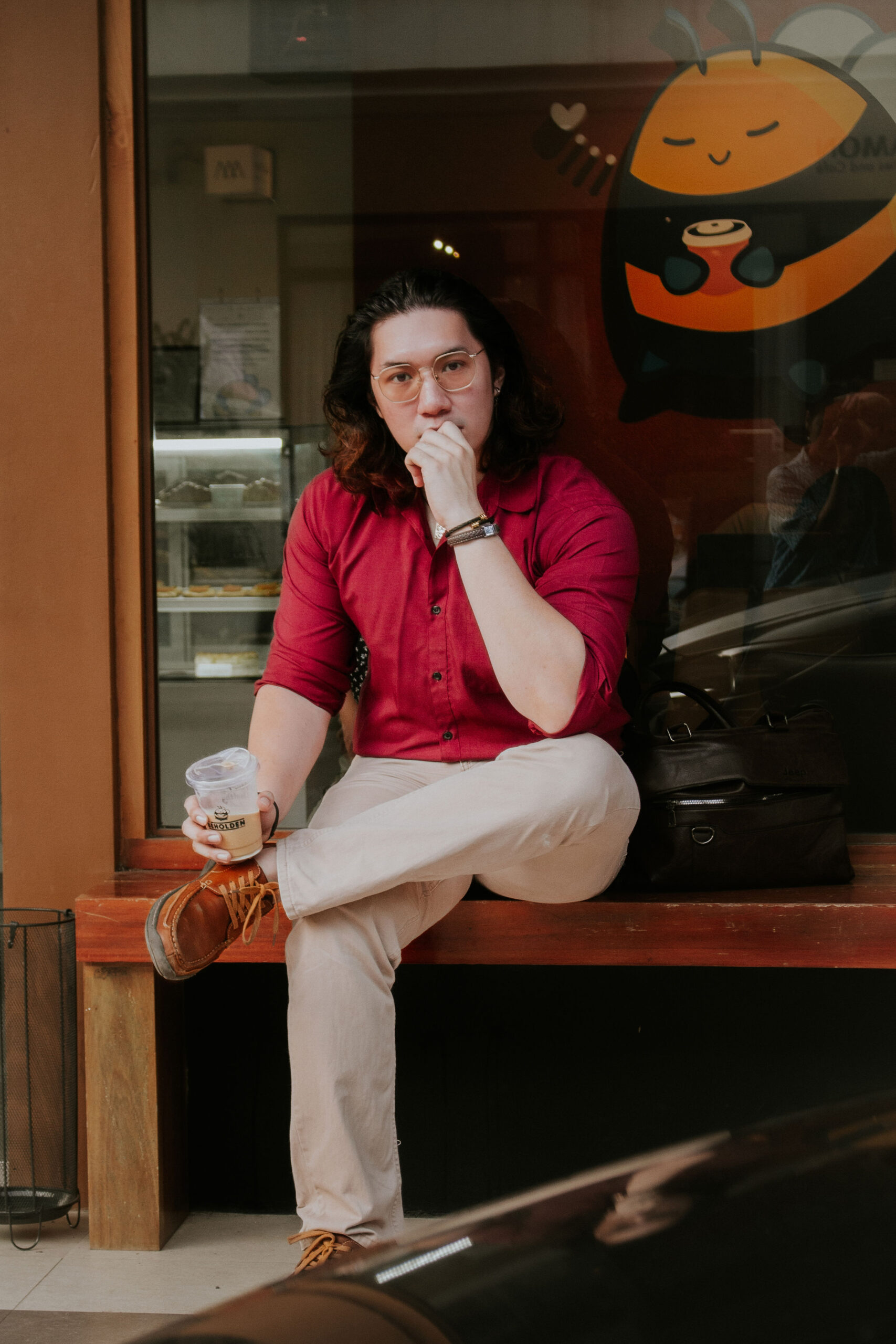 Liam in a red shirt on a wooden café bench, holding an iced coffee