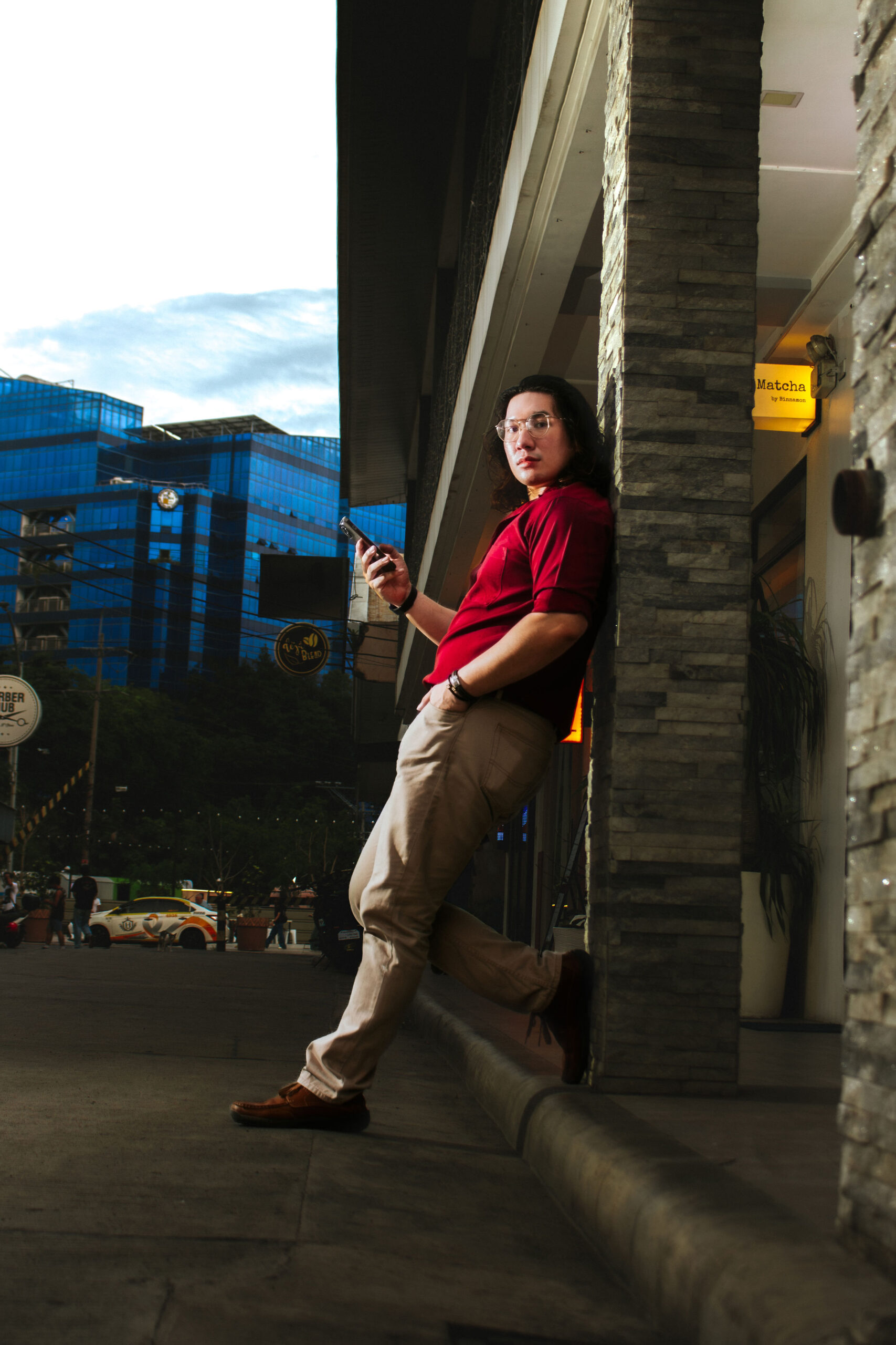 Liam leaning on a stone wall with glass office towers behind